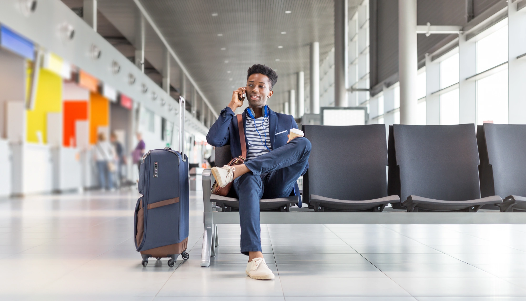 Young man on the phone while sitting at the airport gate with his suitcase and discussing data privacy