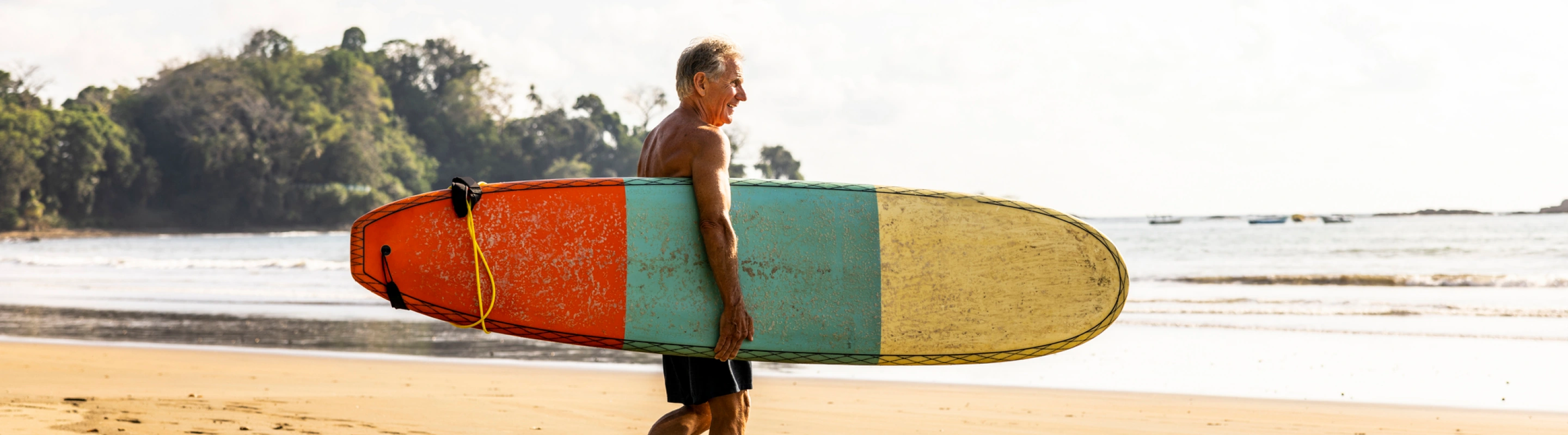 man with travel insurance for Costa Rica on the beach, carrying a surfboard