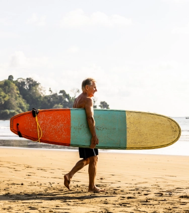 man with travel insurance for Costa Rica on the beach, carrying a surfboard