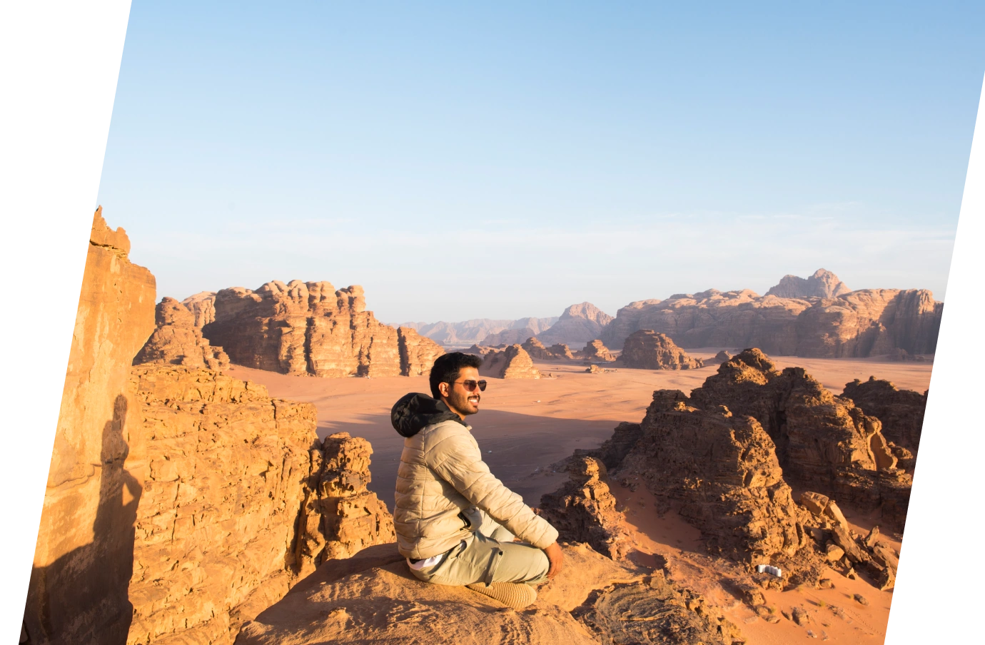 a young man with sunglasses and travel insurance for Jordan enjoys his viewpoint of Wadi Rum's sandstone massifs
