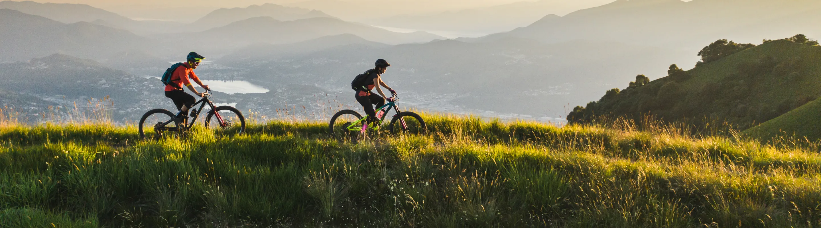 a man and woman with travel insurance for Switzerland bike at the grassy head of a valley above a lake at golden hour