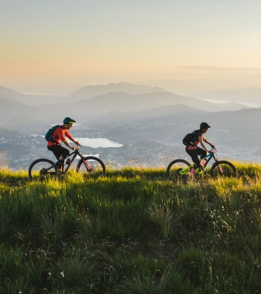 a man and woman with travel insurance for Switzerland bike at the grassy head of a valley above a lake at golden hour