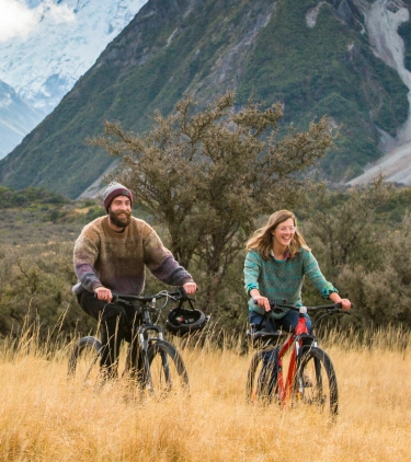 a man and woman biking through Hooker Valley in autumn with travel insurance for New Zealand