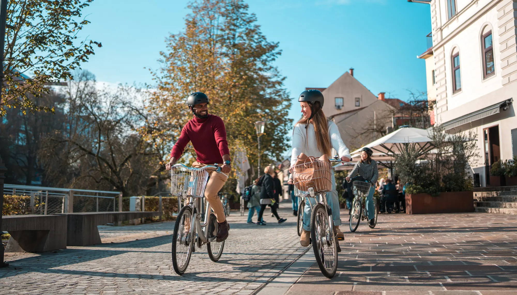 a man and woman wear helmets and bike through town on vacation, following the responsible traveler tips they researched 