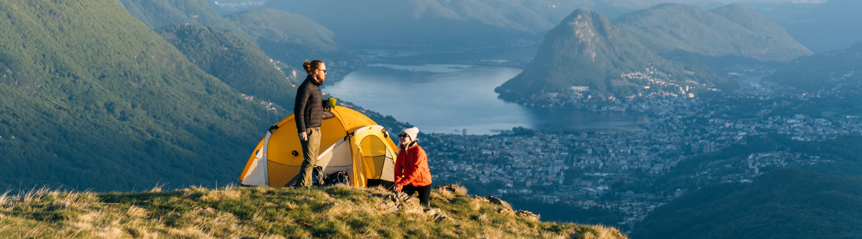 a couple with travel insurance for Switzerland camps on the ledge of a Swiss mountain overlooking a town below
