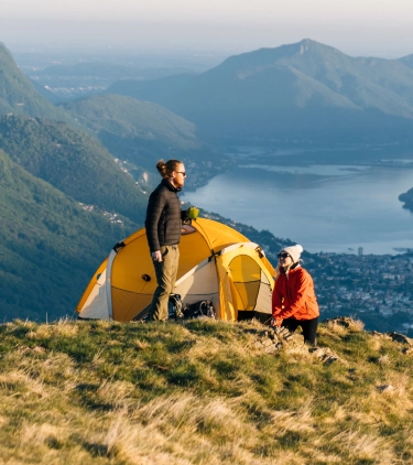a couple with travel insurance for Switzerland camps on the ledge of a Swiss mountain overlooking a town below