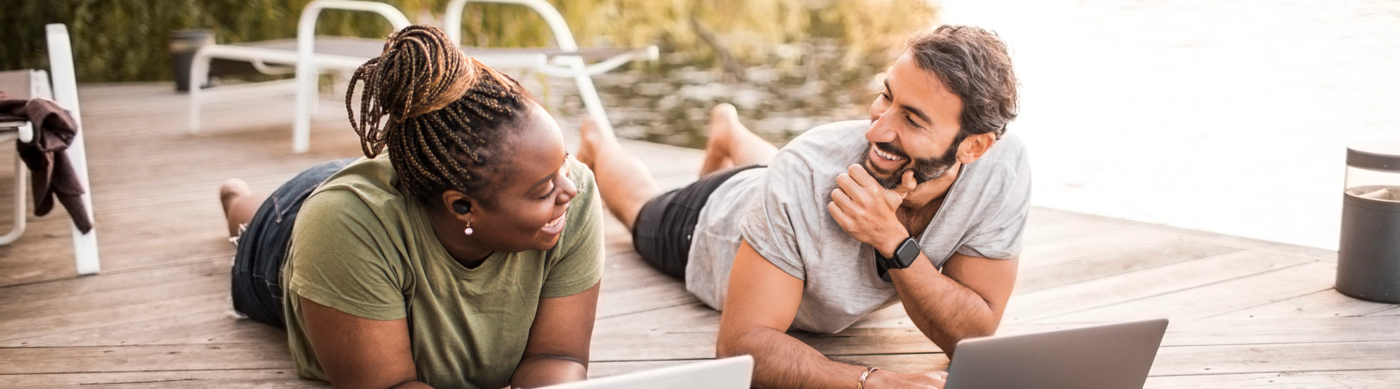 a young man and woman lay on their stomachs on a dock while they work remotely, insured with business travel insurance 