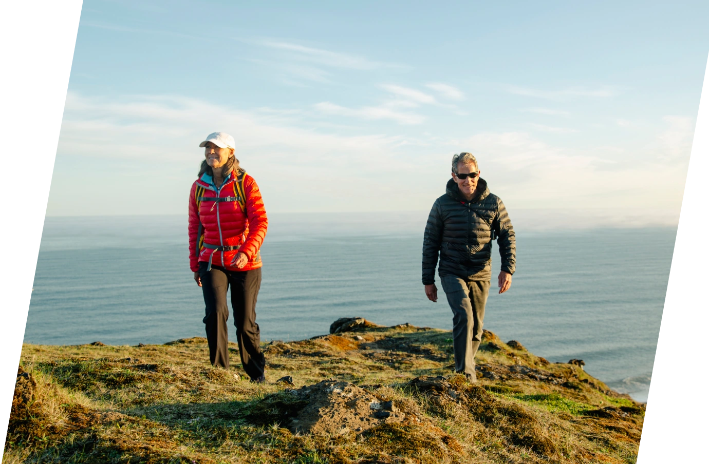 a man and woman hiking with travel insurance for Iceland by the ocean in warm clothes