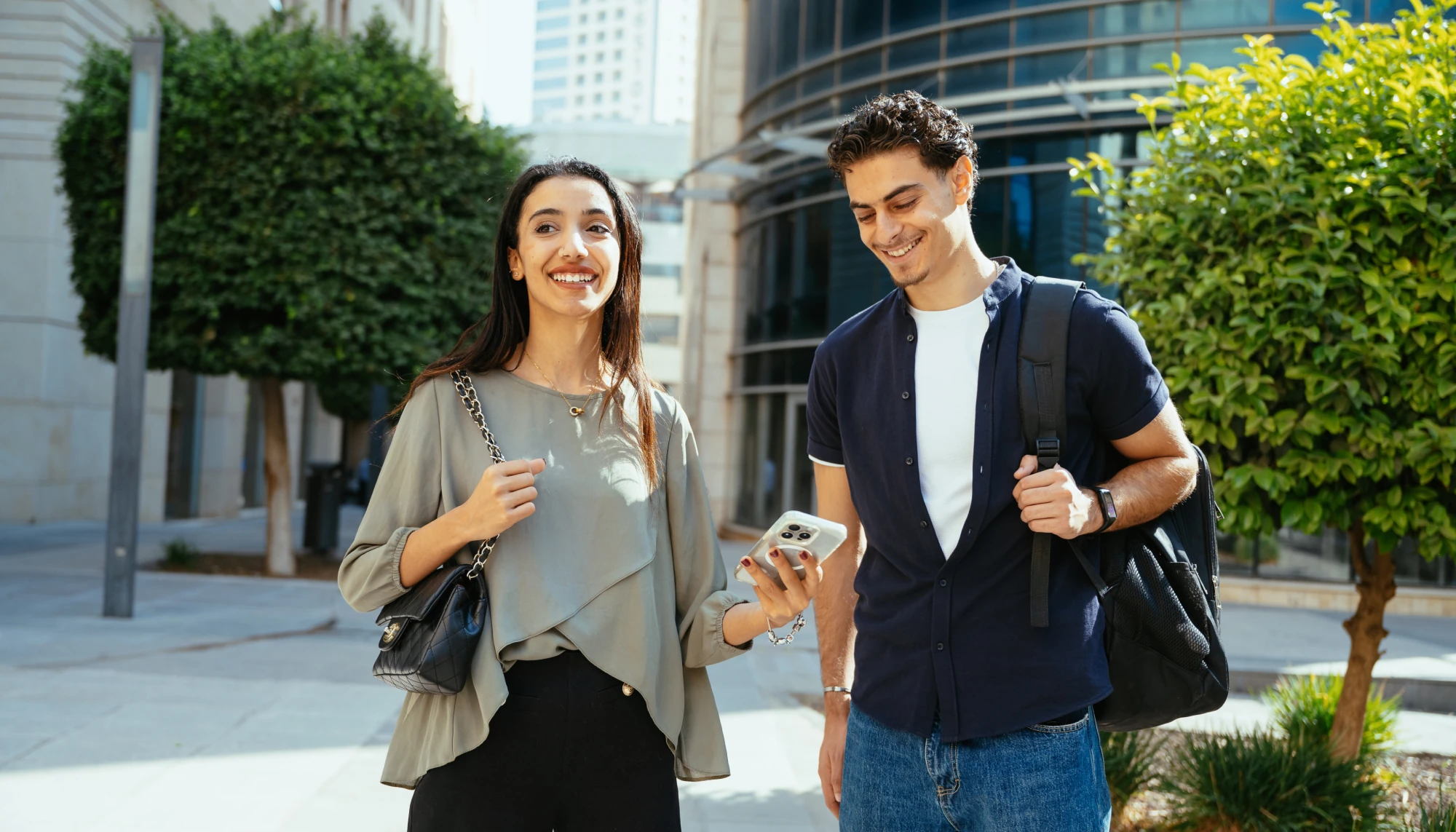 a man looks at a woman's phone in a city setting, where she has a travel app for safer travel pulled up 