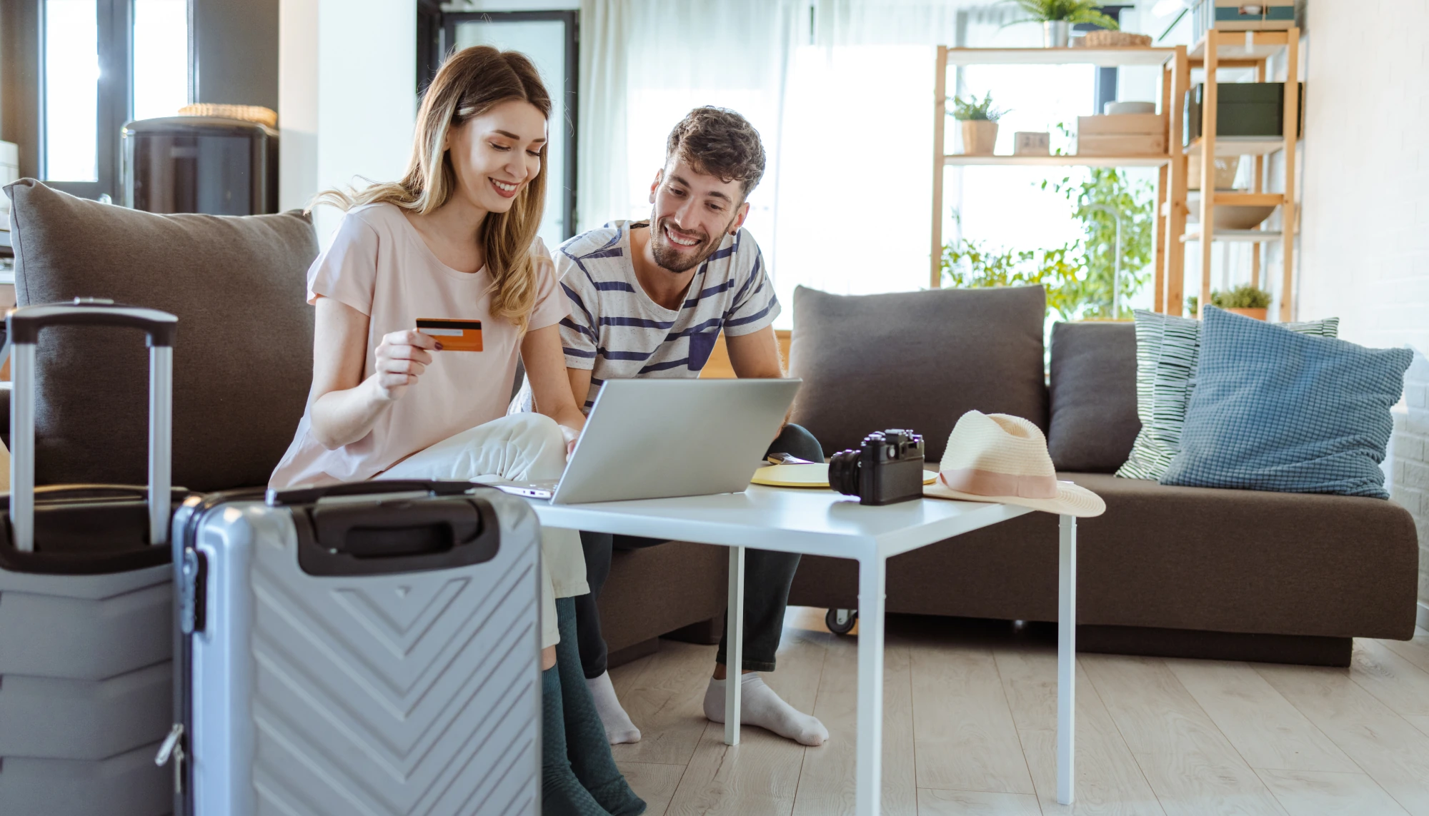 A woman with a suitcase holds a card as she and her partner check a laptop to debunk credit card travel insurance myths