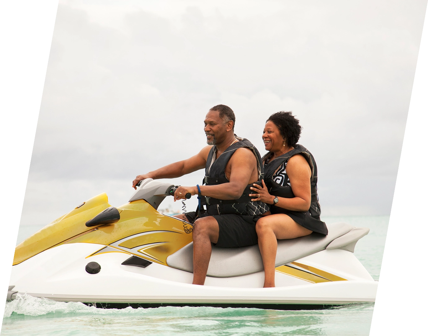 a middle-aged, black couple ride a yellow jet ski together in the ocean, insured with adventure travel insurance 