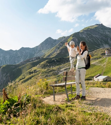 Mother with travel insurance for Germany holding her baby's hands on a bench overlooking the mountains in Bavaria