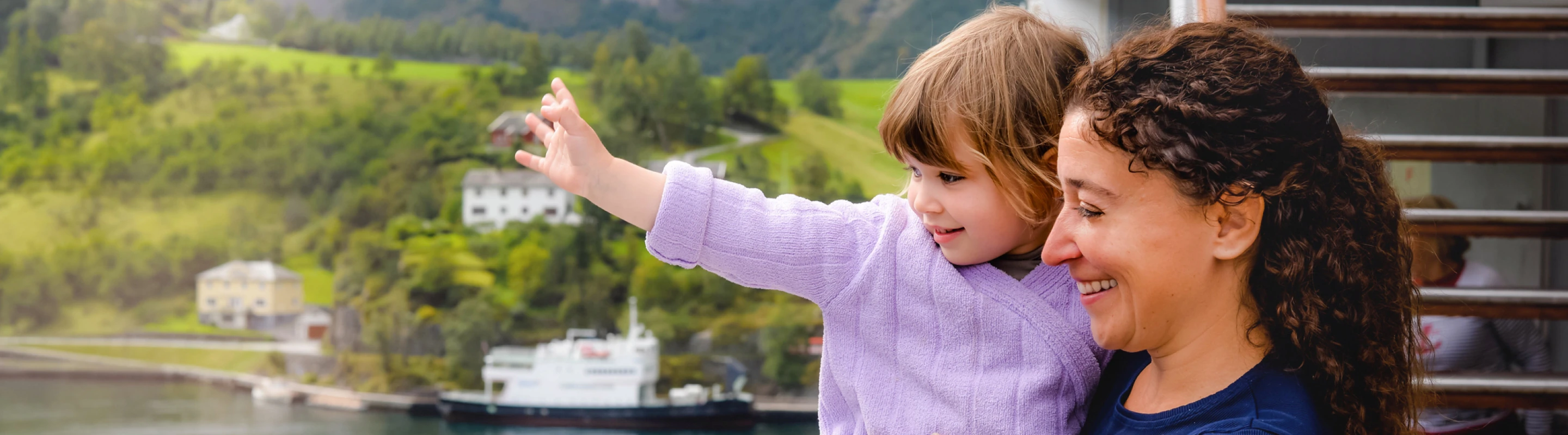 a mother with cruise travel insurance holds her toddler daughter as they stand on their cabin's balcony to soak up views 