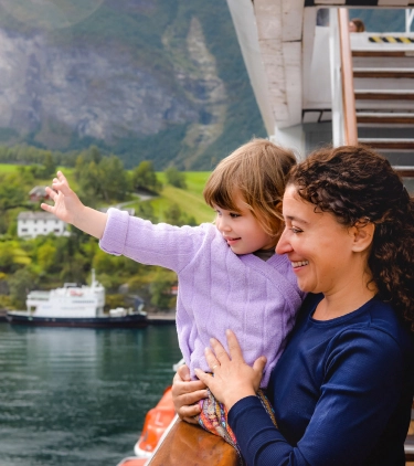 a mother with cruise travel insurance holds her toddler daughter as they stand on their cabin's balcony to soak up views 