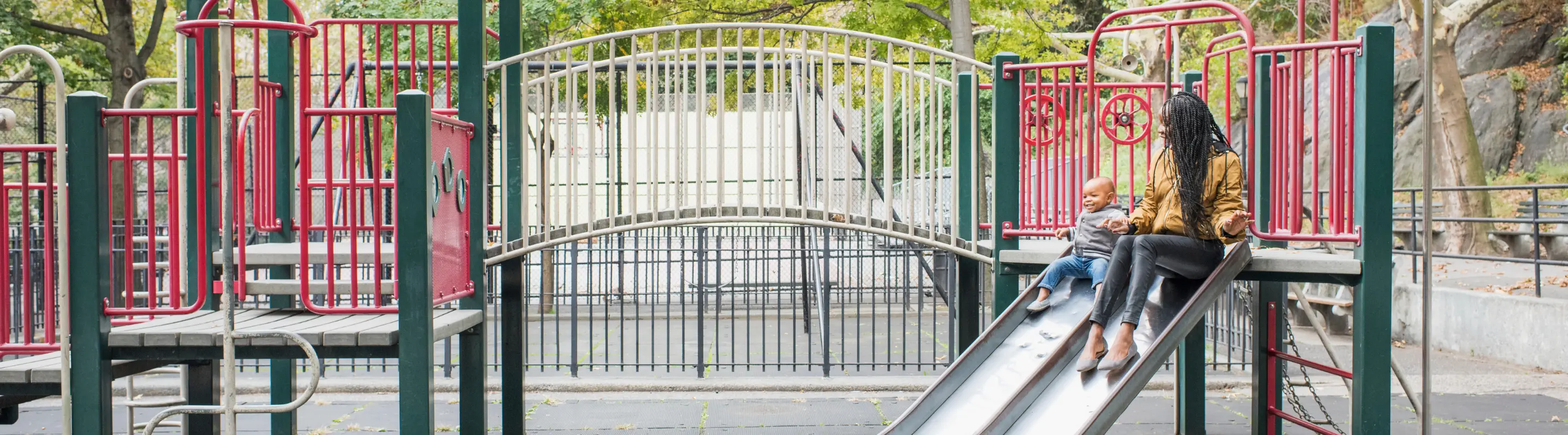 Mother with travel insurance for New York playing with her young son on a playground in the city
