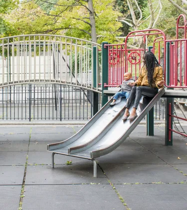 Mother with travel insurance for New York playing with her young son on a playground in the city