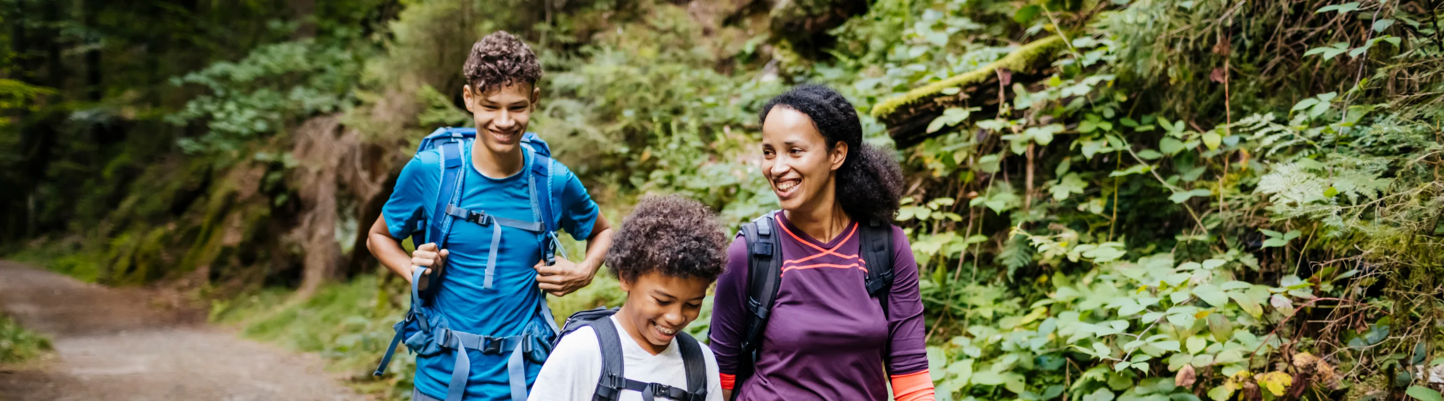 a young mother with backpacker travel insurance hikes through a forest with her two sons (one a teen and the other a child)