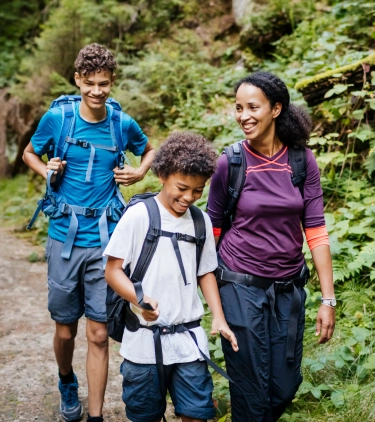 a young mother with backpacker travel insurance hikes through a forest with her two sons (one a teen and the other a child)
