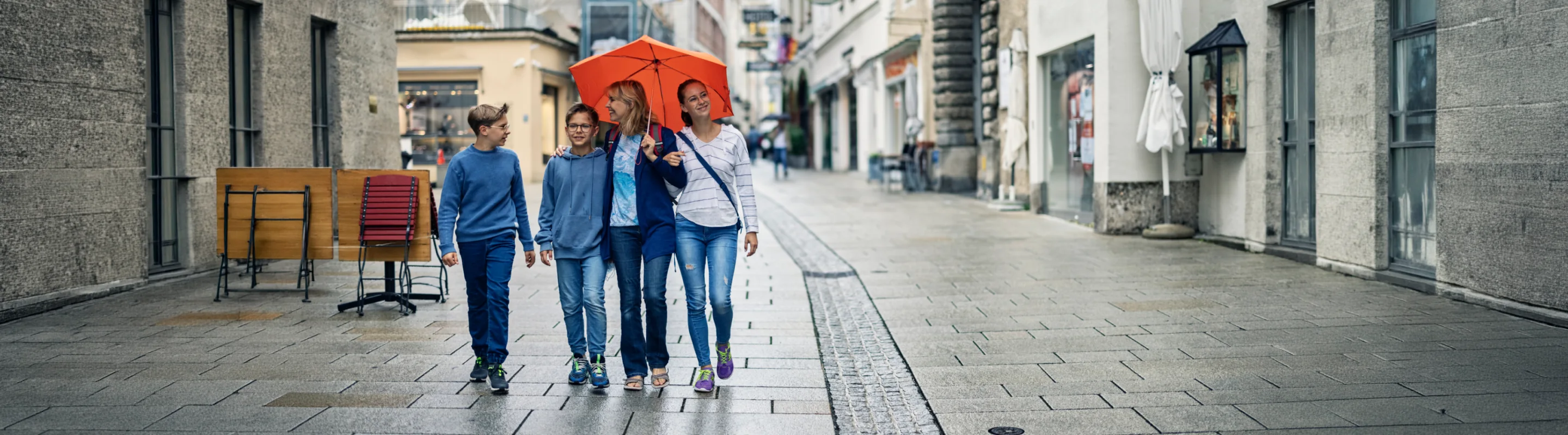 a mother with her teenage kids, walking through a rainy Austrian town and protected by travel insurance for Austria 
