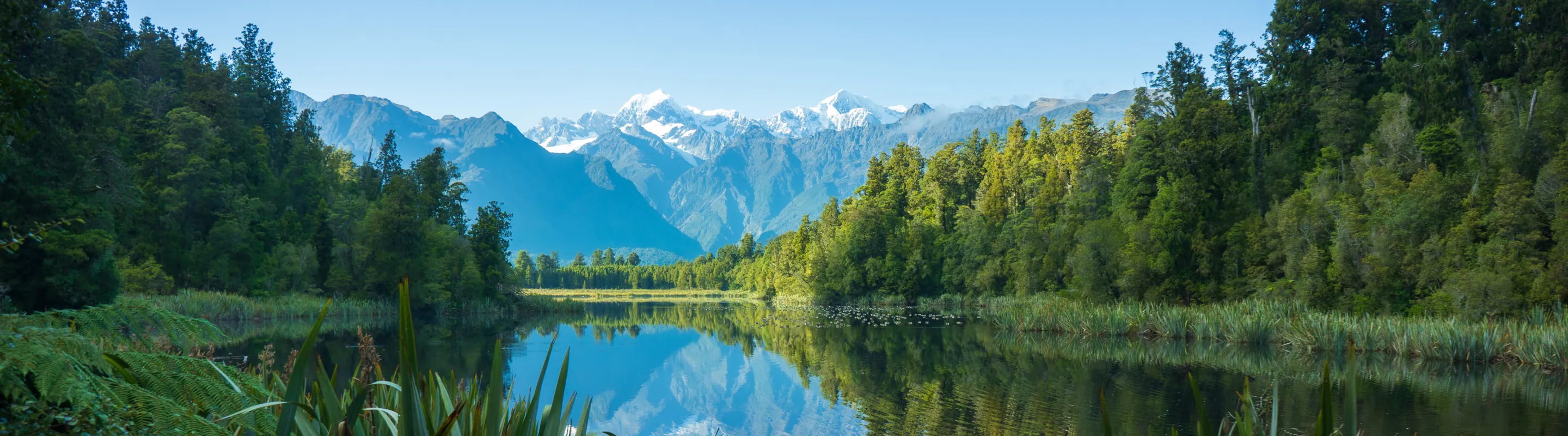 view of Lake Matheson with trees on each side and mountains in the background, highlighting travel insurance for New Zealand