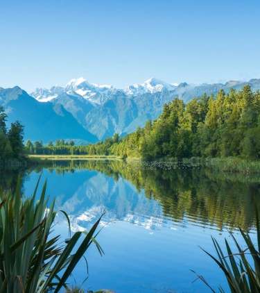 view of Lake Matheson with trees on each side and mountains in the background, highlighting travel insurance for New Zealand