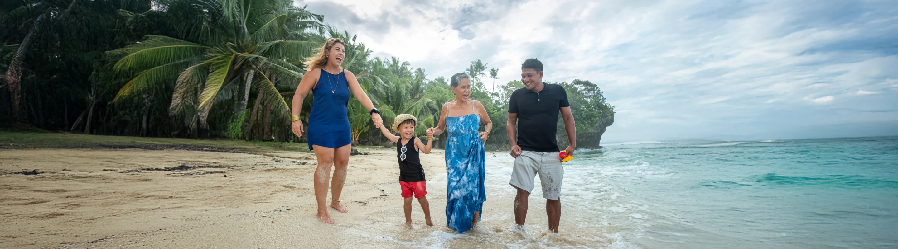 a multi-generational family with travel insurance for the Philippines, walking on a beach with palm trees on the shoreline