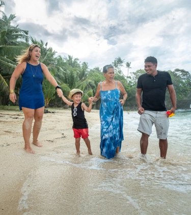 a multi-generational family with travel insurance for the Philippines, walking on a beach with palm trees on the shoreline