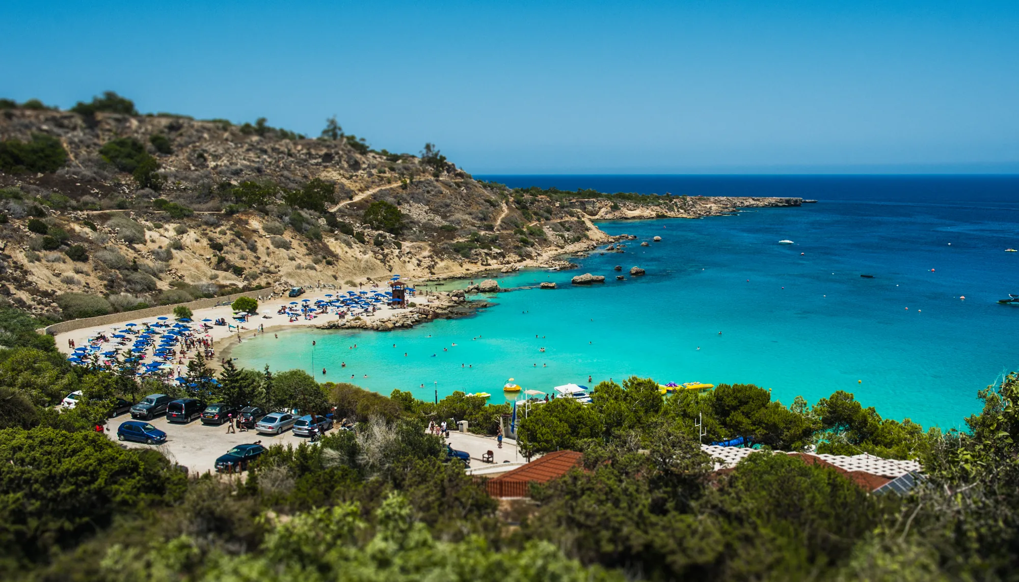 a Greek resort with turquoise water, a white-sand beach, and umbrellas, prompting: "are all-inclusive resorts worth it?"