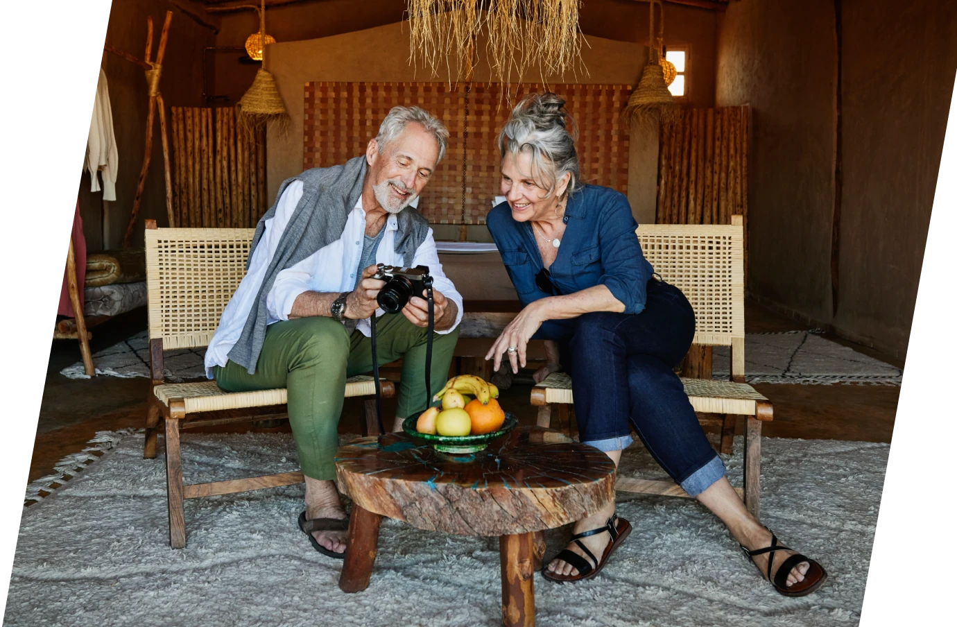 an older couple with travel insurance for Morocco looks at photos on a large camera in their earthy, rustic hotel room