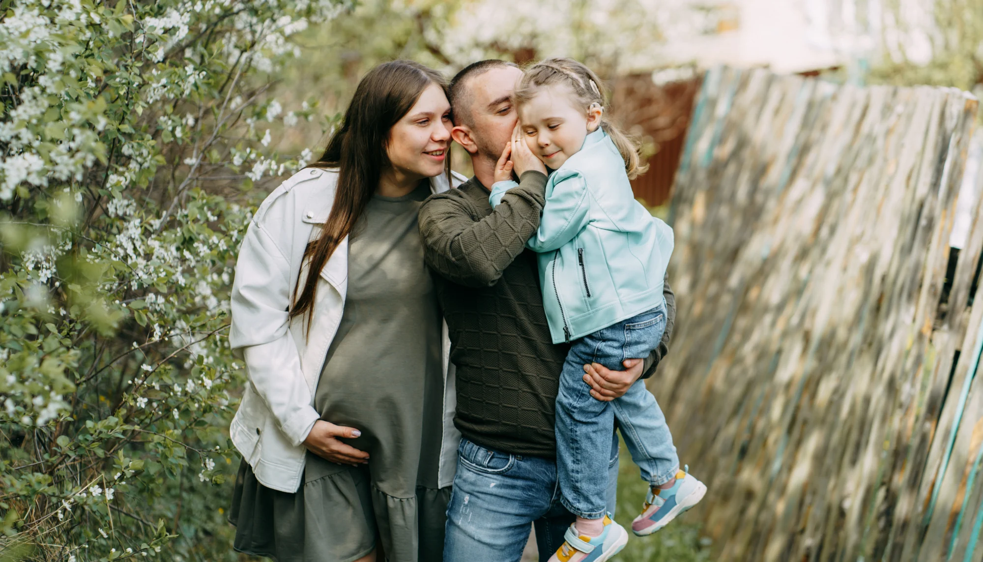 Father whispering into his young daughter's ear and standing next to his wife traveling during pregnancy