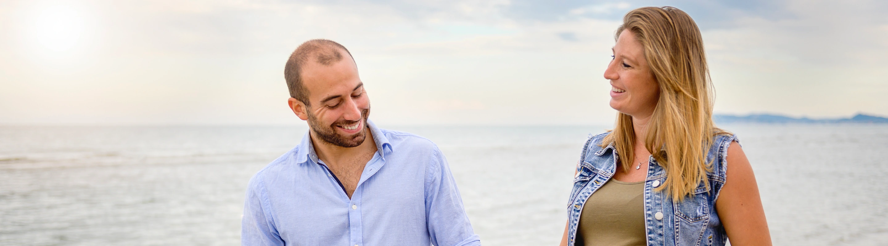 an expecting couple with travel insurance for pregnancy enjoy a walk outdoors in a seaside, casual setting