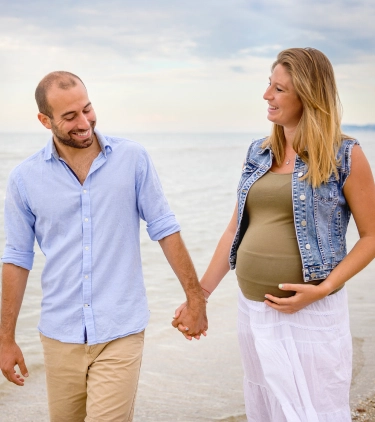 an expecting couple with travel insurance for pregnancy enjoy a walk outdoors in a seaside, casual setting