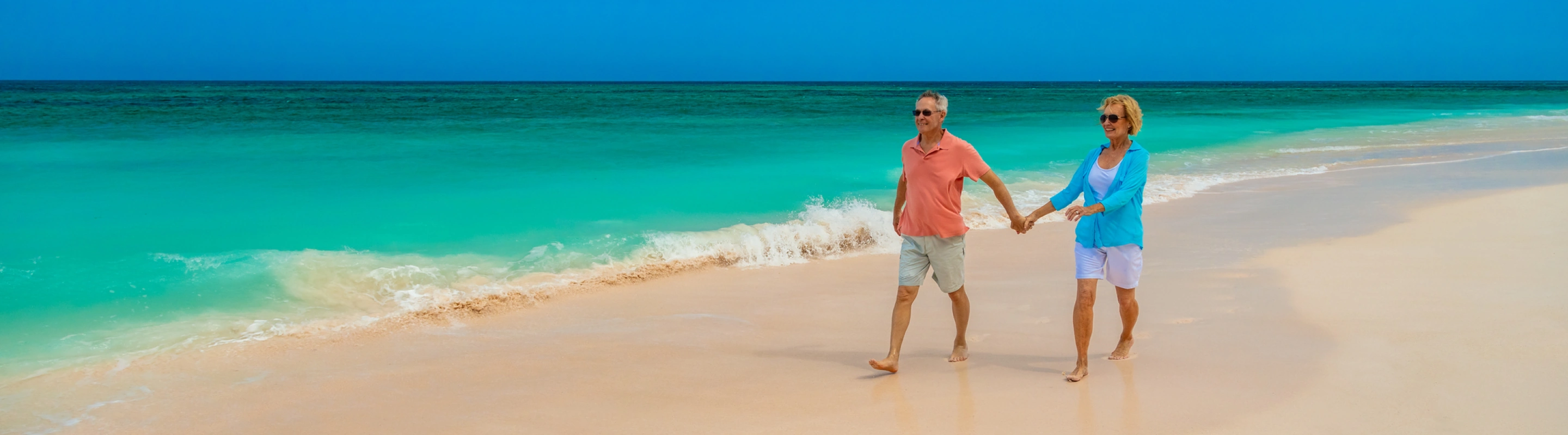 Senior couple with travel insurance for the Bahamas holding hands and walking on the beach