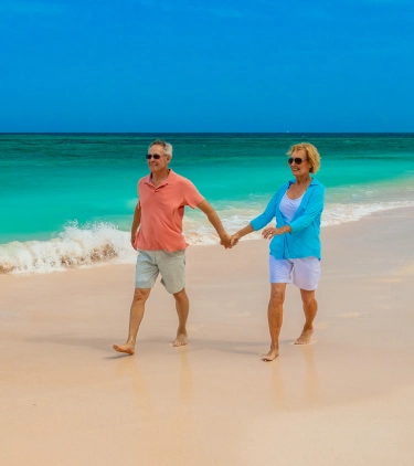 Senior couple with travel insurance for the Bahamas holding hands and walking on the beach