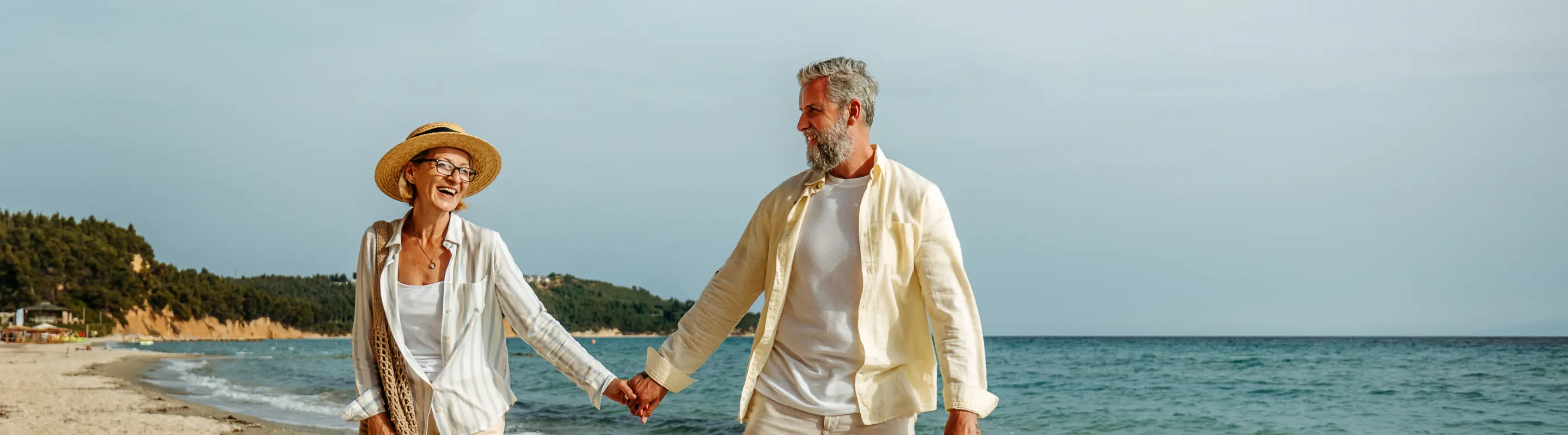 Senior couple with travel insurance for Greece holding hands and walking on the beach