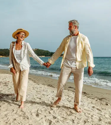 Senior couple with travel insurance for Greece holding hands and walking on the beach