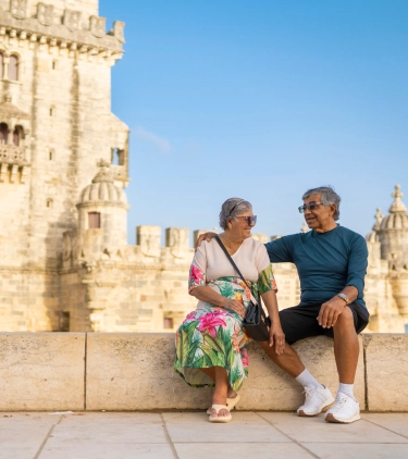 Senior couple with travel insurance for Portugal embracing in Lisbon with Belem Tower in the background