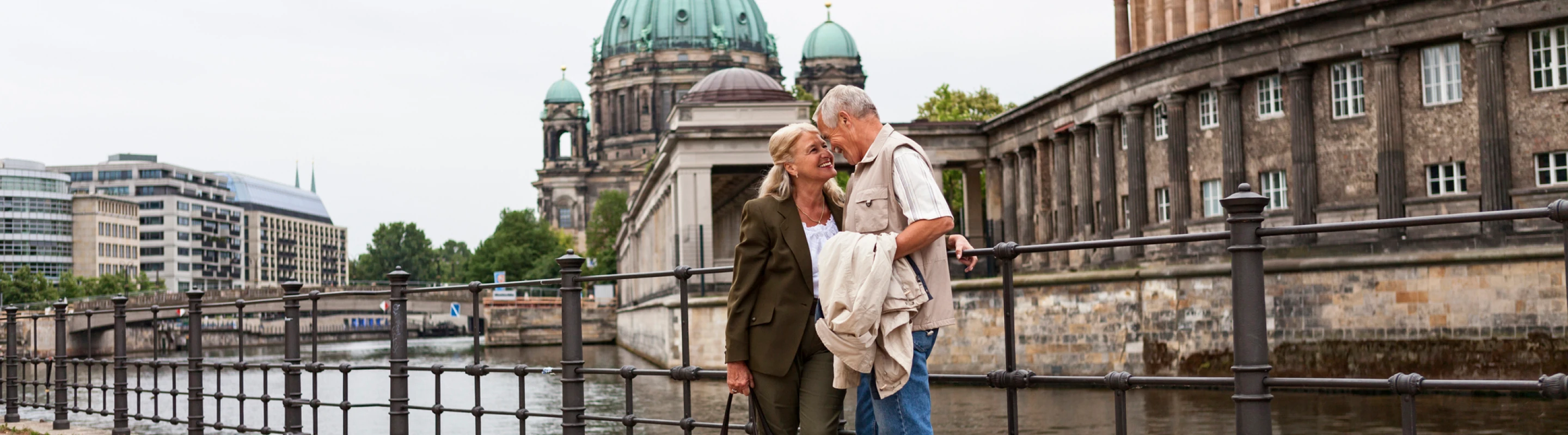 Senior couple with travel insurance for Germany embracing in front of a waterway with the Berlin Cathedral in the background