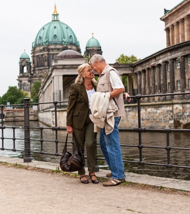 Senior couple with travel insurance for Germany embracing in front of a waterway with the Berlin Cathedral in the background