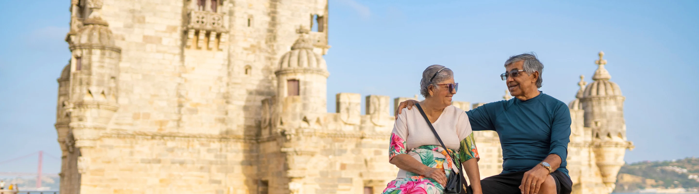 Senior couple with travel insurance for Portugal sitting on a rooftop with a historic building in the background in Lisbon