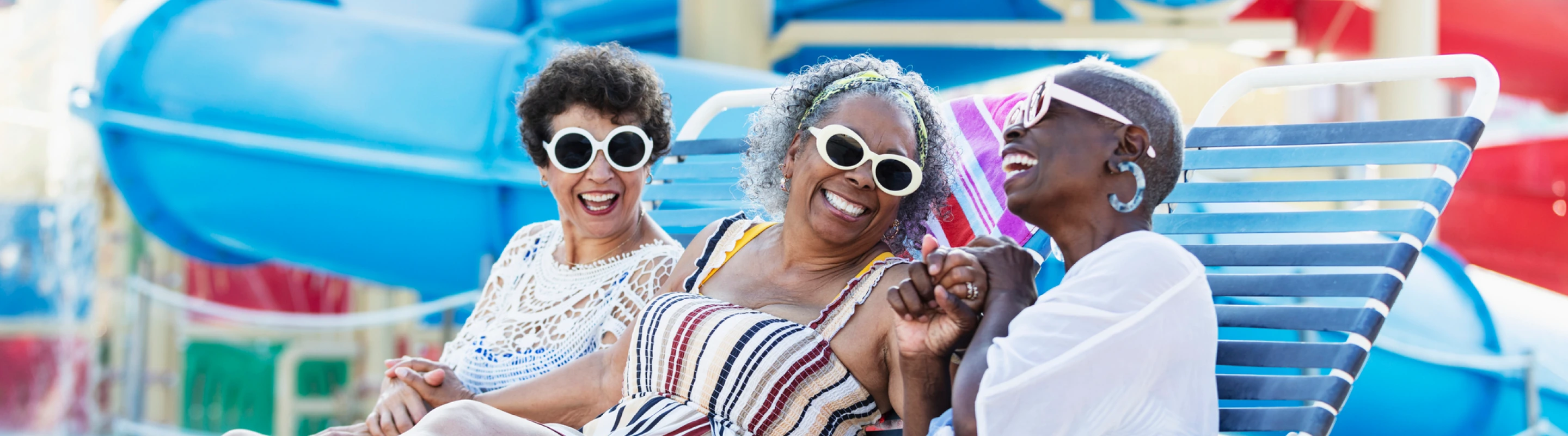 Three senior women with travel insurance for Florida laughing on lounge chairs at a waterpark