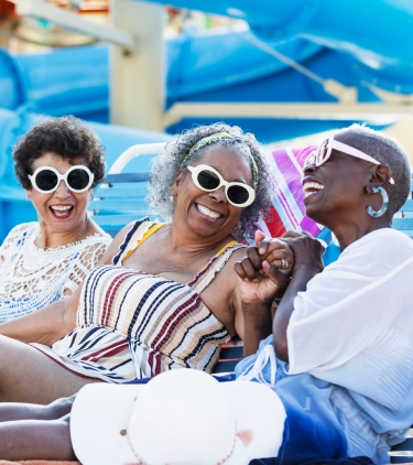 Three senior women with travel insurance for Florida laughing on lounge chairs at a waterpark