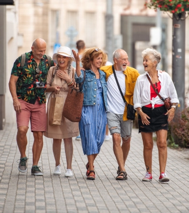 six older adults with group travel insurance laugh and chat as they walk down a city street on vacation