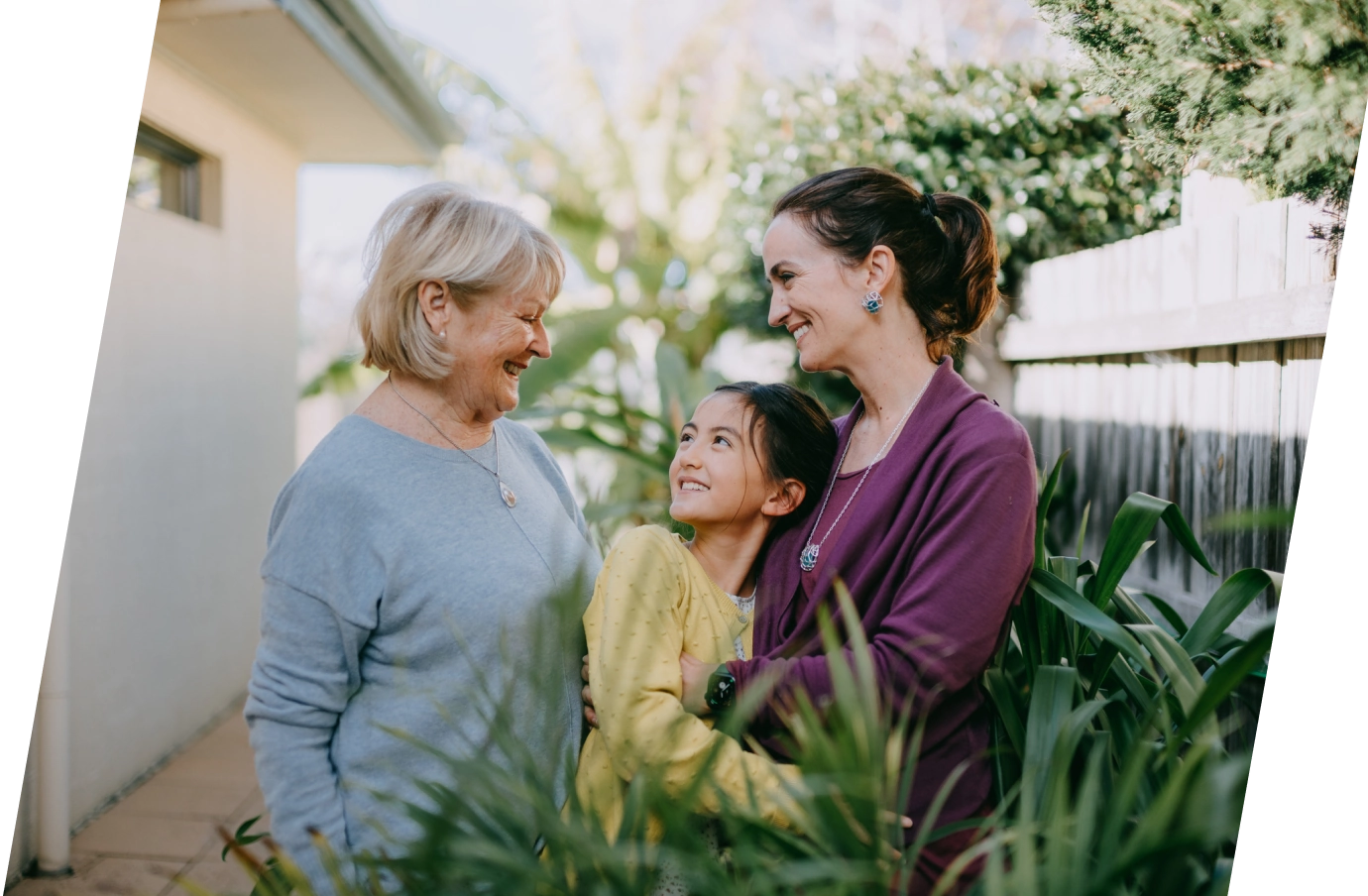 Grandmother with affordable travel insurance smiling with her daughter and granddaughter outside of a house