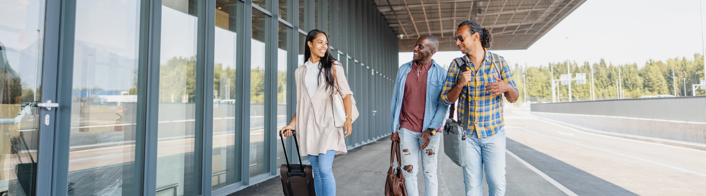 three young adults with group travel insurance walk past an airport’s exterior with their luggage