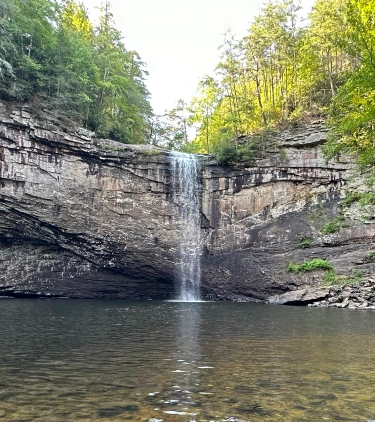 Waterfall flowing into the river in a forest in Sequatchie, highlighting travel insurance for Tennessee