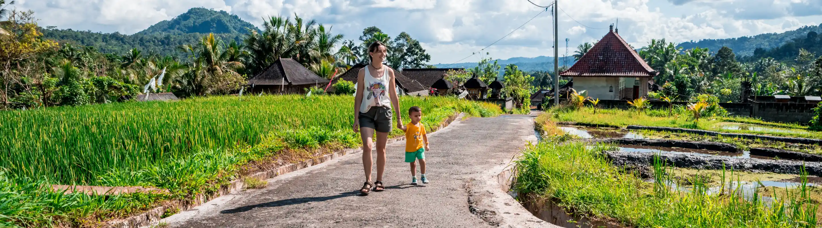 Woman with travel insurance for Bali holding hands with a young child and walking down a path in a village