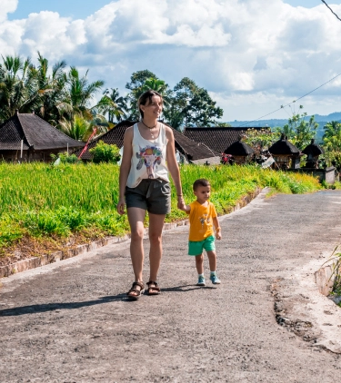 Woman with travel insurance for Bali holding hands with a young child and walking down a path in a village