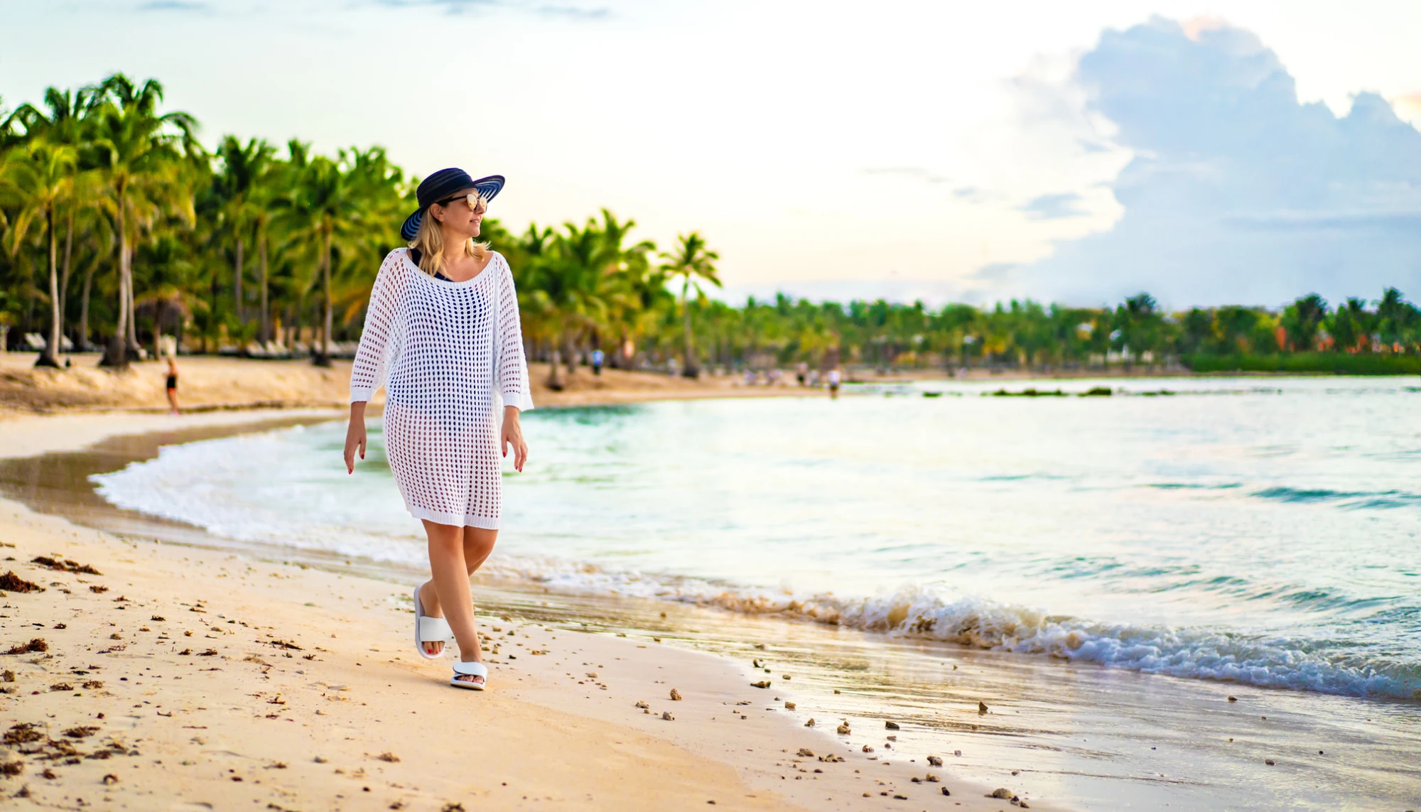 a woman strolling along a beach with palm trees in the background, an attraction highlighted in many Caribbean travel guides