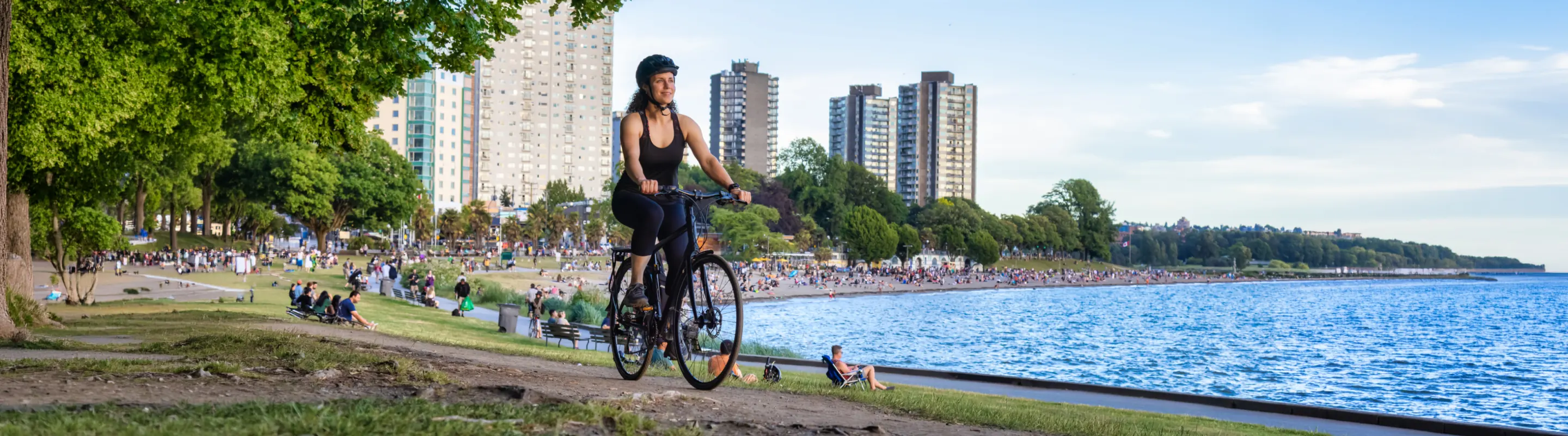 Young woman with travel insurance for Canada biking in a park with Vancouver in the background